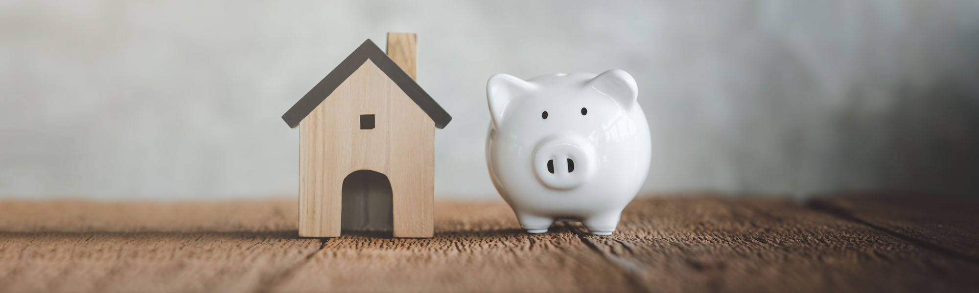 white piggy bank with wooden house on wood table